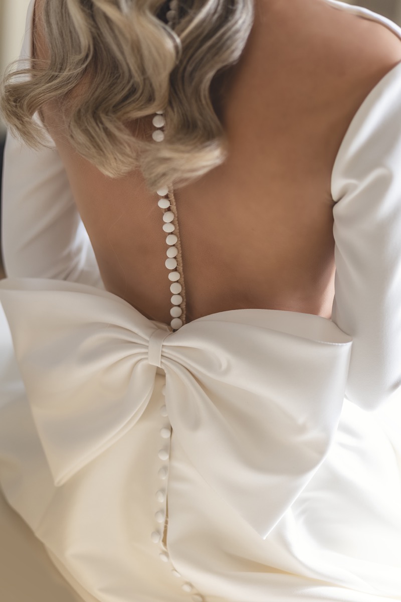 Close-up of bride's wedding dress with pearl button back and large silk bow, Northern Ireland wedding photography by Annette Burke
